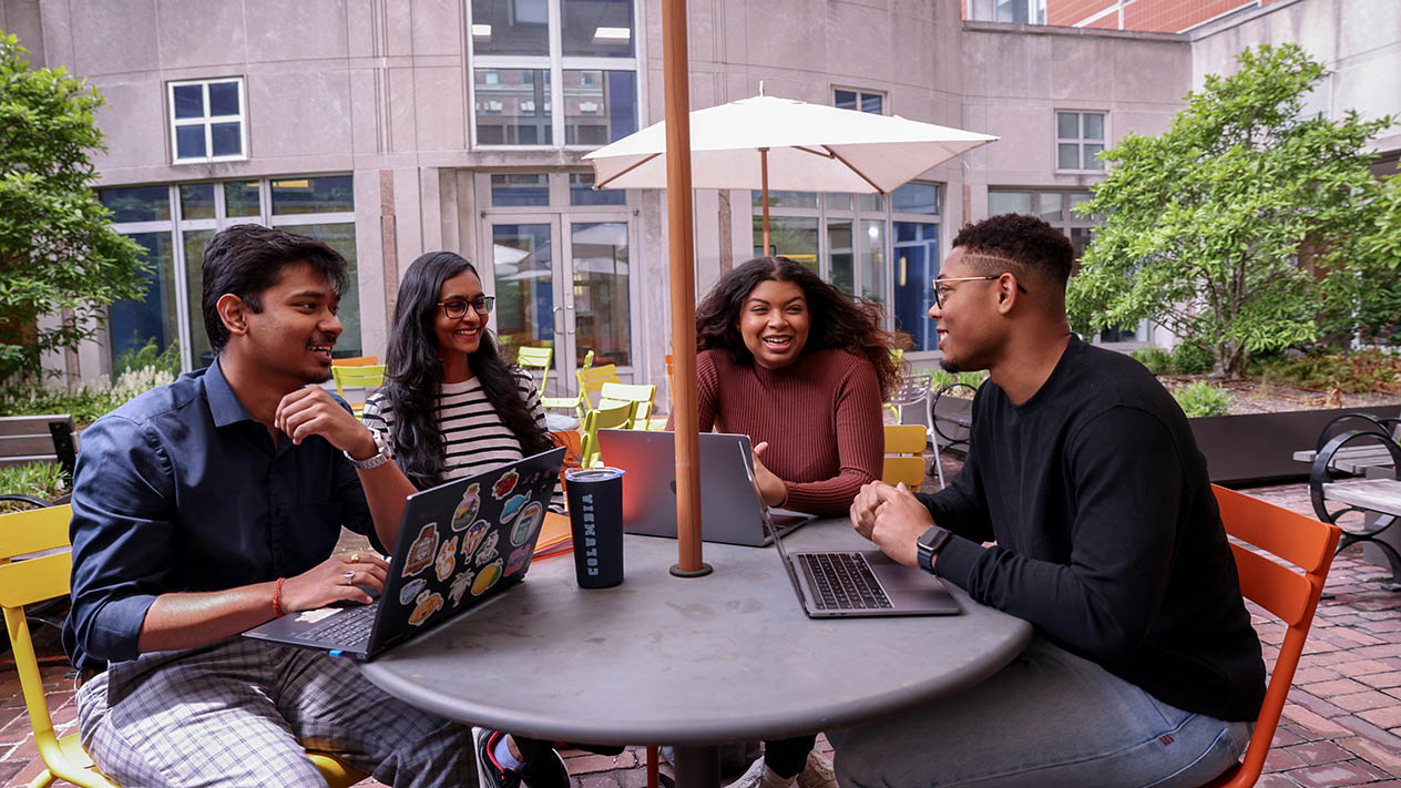 Four students sit and talk outdoors on Columbia's campus.