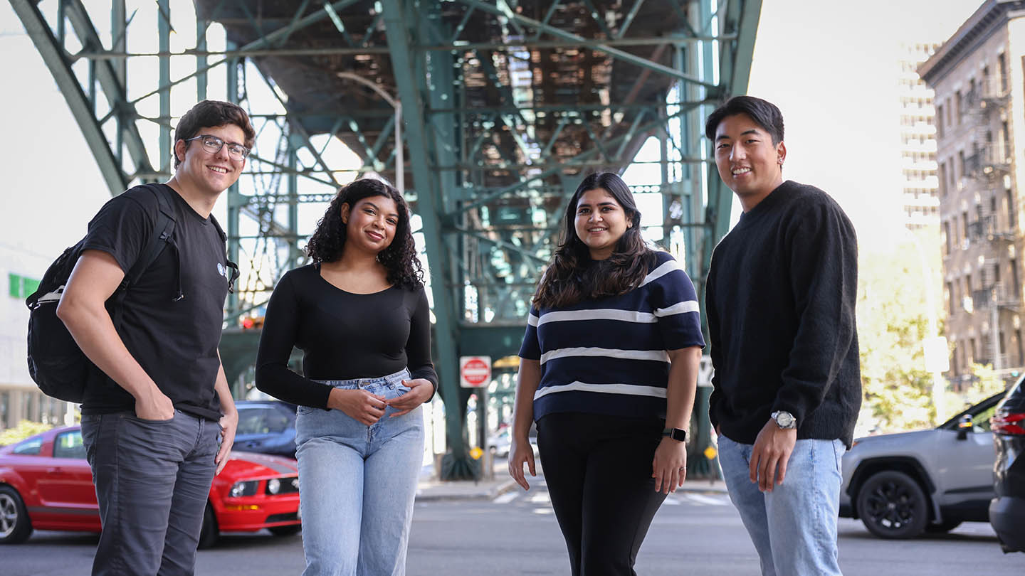 Four students pose under a large bridge in New York City.