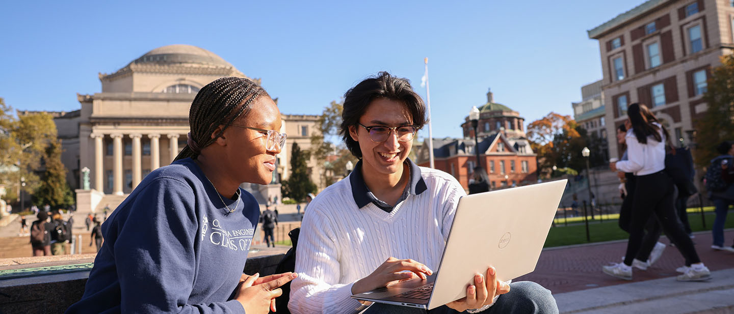 Two students work together on a laptop outdoors on Columbia University's campus.