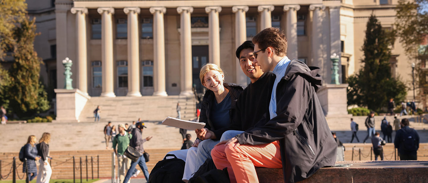 Three students smiling outdoors on Columbia University's campus.