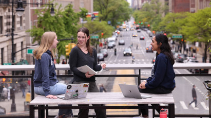 Three students work together on a bridge over a busy New York City street.